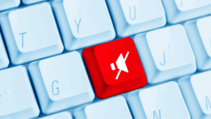 Teclado de computadora con una tecla destacada en rojo que tiene el símbolo de un parlante, tachado.